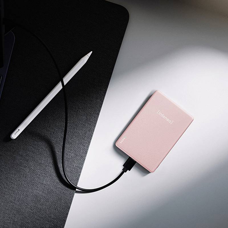 Une batterie externe rose portant l'étiquette « Intenso » est connectée à un appareil, posée sur une surface sombre à côté d'un stylet blanc.