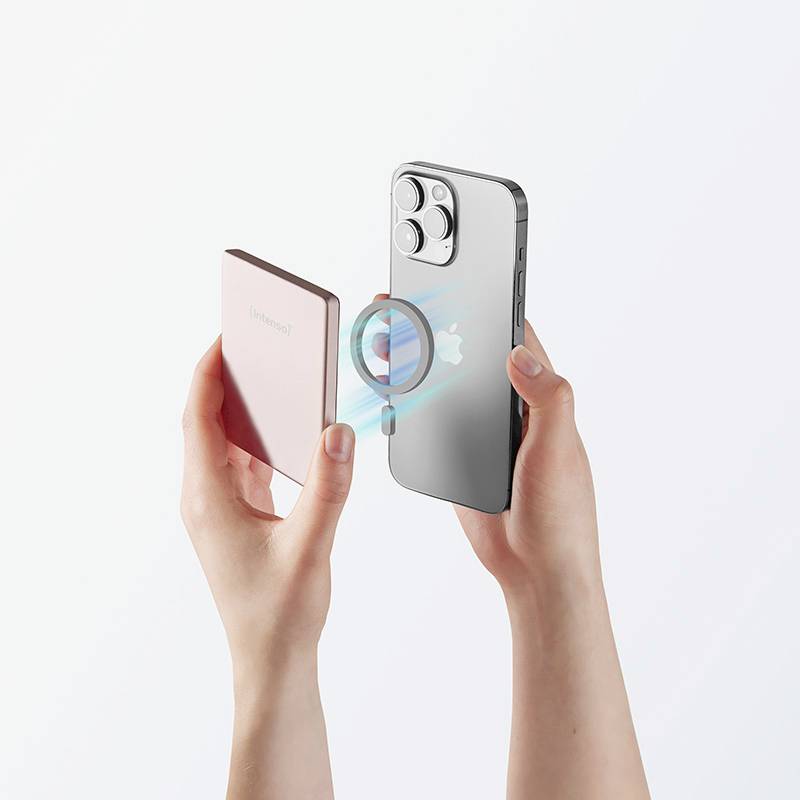 Deux mains tenant une batterie externe magnétique rose en la fixant à un smartphone argenté avec un logo Apple visible, doté de trois caméras.