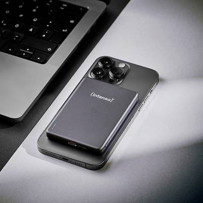 Une batterie externe élégante portant la marque « Intenso » repose sur un smartphone à côté d'un ordinateur portable, suggérant un environnement technologique ou une situation de recharge.