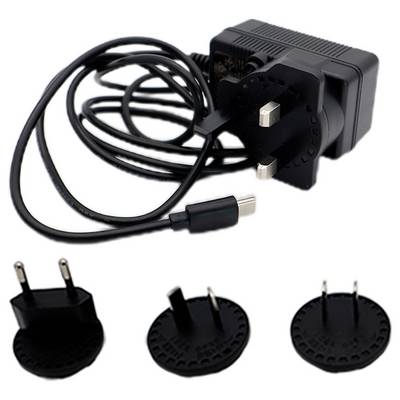 Un adaptateur secteur noir avec un câble et trois fiches interchangeables : UK, UE et US, adapté aux différentes prises internationales.