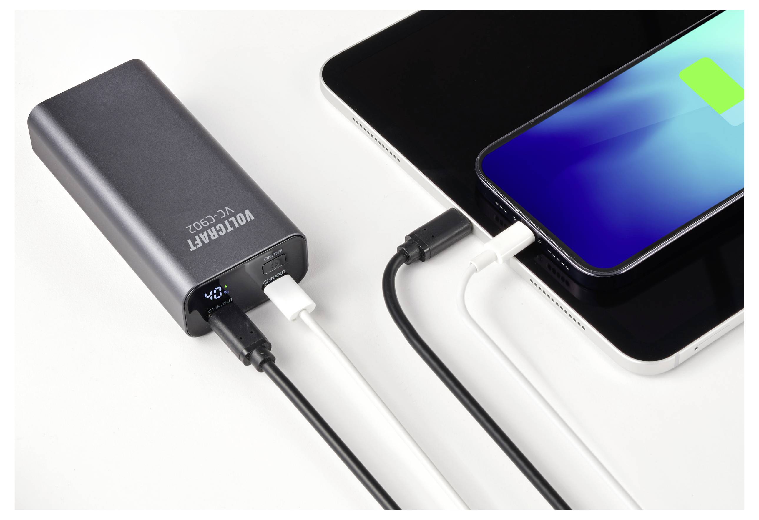 Une batterie externe charge simultanément un smartphone et une tablette. L'écran du téléphone affiche un symbole de charge.