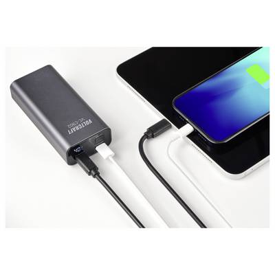 Une batterie externe charge simultanément un smartphone et une tablette. L'écran du téléphone affiche un symbole de charge.