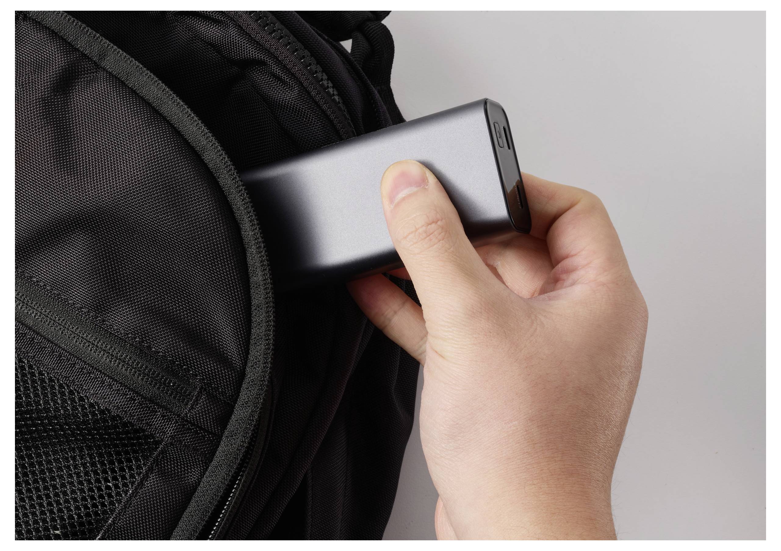 Une main place une batterie externe portable dans la poche avant d'un sac à dos noir, soulignant la commodité et la portabilité pour charger les appareils en déplacement.