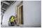 Un ouvrier du bâtiment portant un gilet jaune et un casque bleu examine un chambranle dans un bâtiment en cours de construction, vérifiant l'alignement et la stabilité.