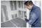 Une personne tenant un appareil, inspectant une pièce partiellement construite ou rénovée avec des murs inachevés et des prises électriques visibles.