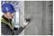 Un ouvrier du bâtiment portant un casque de chantier bleu et un gilet de sécurité utilise un outil de mesure sur un mur en béton à l'intérieur d'un bâtiment en construction.