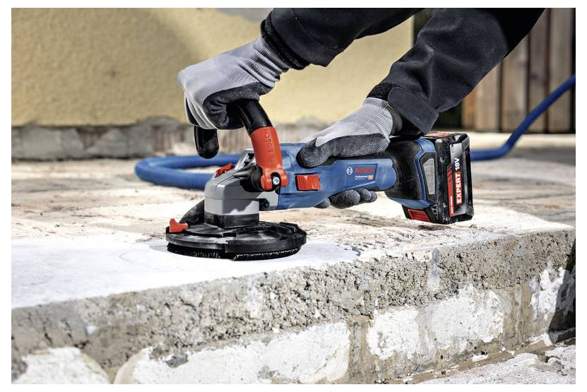 Une personne utilise une meuleuse à béton Bosch sur une surface en béton brut, en la lissant. L'outil est sans fil avec des accents rouges et bleus visibles.