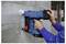 Une personne utilise un cloueur à béton Bosch bleu pour fixer du matériau sur un mur en béton dans un environnement de construction.