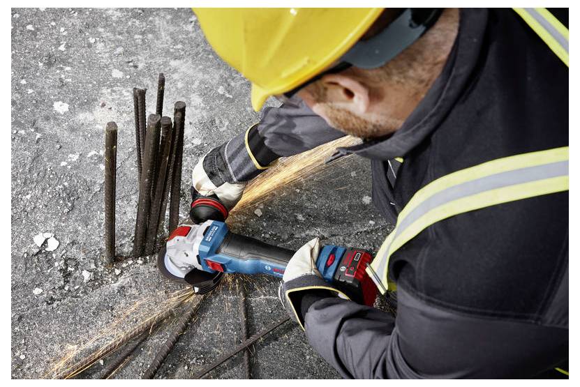 Un ouvrier du bâtiment portant un équipement de protection utilise une meuleuse d'angle pour couper des tiges métalliques dépassantes sur une surface en béton, provoquant des étincelles.