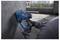 Une personne utilise un outil électrique professionnel Bosch pour percer un mur en béton sur un chantier de construction, avec des immeubles de la ville en arrière-plan.