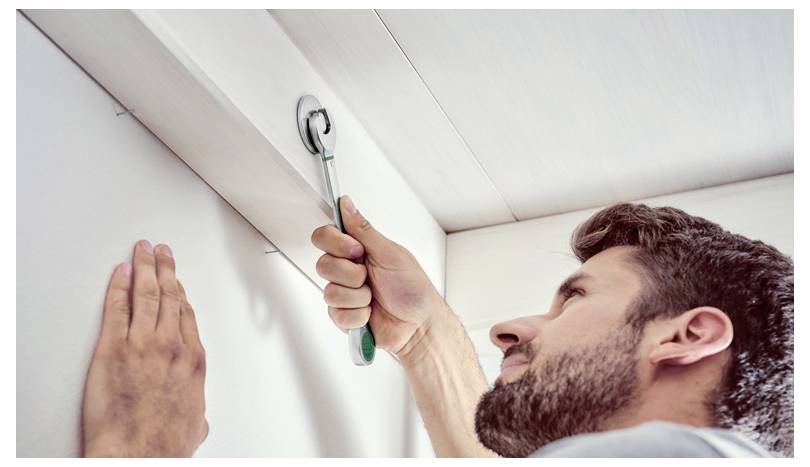 Une personne utilise une clé à cliquet pour assembler un panneau de plafond blanc, concentrée et manifestant des efforts pour serrer un boulon.
