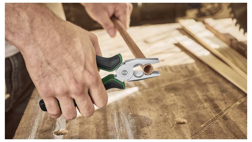 Une personne utilisant des pinces pour saisir un petit tuyau sur une surface en bois, suggérant un projet de menuiserie ou de bricolage en cours.