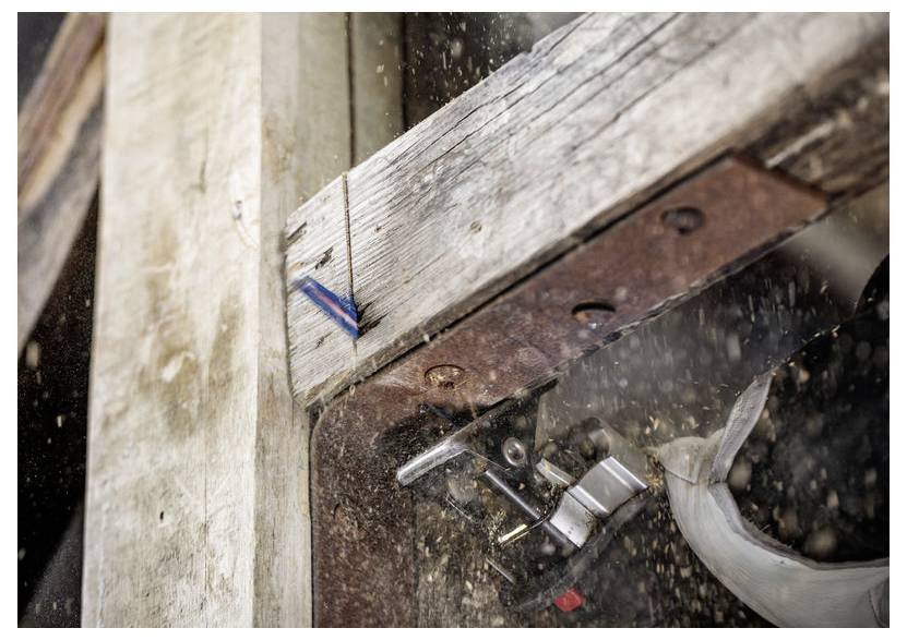 Un plan rapproché montre une charnière de porte en train d'être découpée avec un outil électrique, créant des étincelles et de la sciure, mettant en valeur l'action et le savoir-faire.