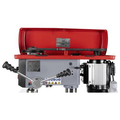 Une machine industrielle rouge et grise avec des leviers et un moteur, utilisée pour des opérations mécaniques, comportant des étiquettes d'avertissement sur son corps.