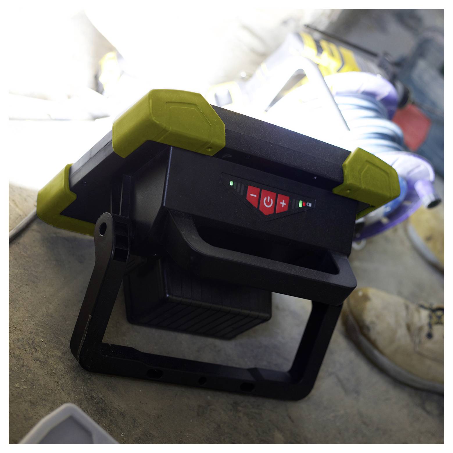 «Lampe de travail LED sur le sol d'un chantier de construction, montrant les boutons de mise en marche et de réglages. À proximité se trouvent des bottes de chantier et des outils.»