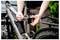 Une personne ajustant le collier de serrage de la tige de selle d'un vélo gris. Des mains sont en train de serrer un boulon sur le collier, indiquant un entretien ou une préparation pour une sortie à vélo.