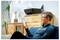 Un homme assis sur un canapé, souriant en regardant un smartphone. Une imprimante multifonction est visible en arrière-plan. Le décor est un salon douillet.