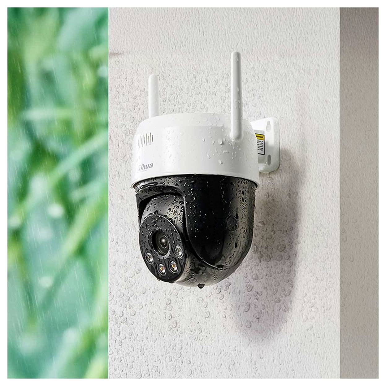 Une caméra de sécurité extérieure blanche et noire fixée à un mur, recouverte de gouttelettes d'eau, avec un arrière-plan vert flou sur la gauche.