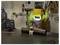 Un soudeur portant un équipement de protection et un casque jaune travaille sur un tuyau métallique dans un atelier, avec des étincelles de soudure visibles.