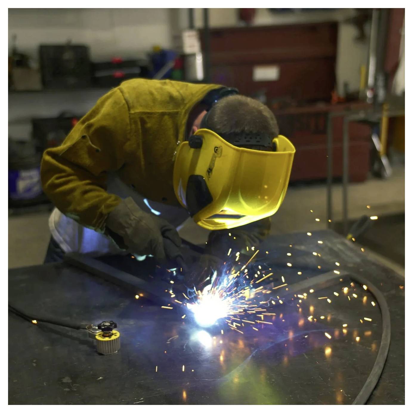 Une personne portant un équipement de protection soude du métal, avec des étincelles vives et une flamme incandescente, dans un environnement industriel.