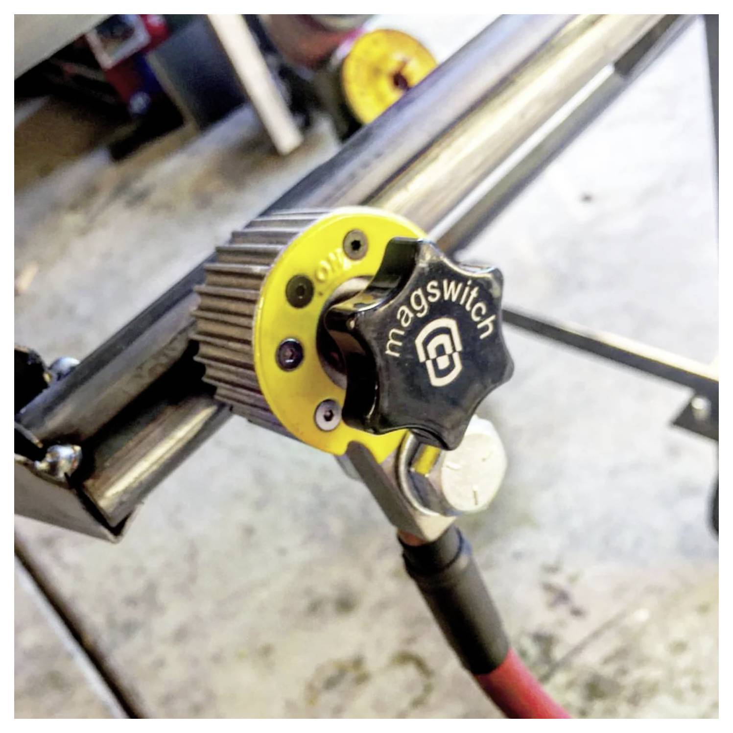 Un interrupteur magnétique jaune et noir portant l'étiquette 'magswitch' est fixé à une barre métallique, probablement utilisé dans un environnement d'atelier.