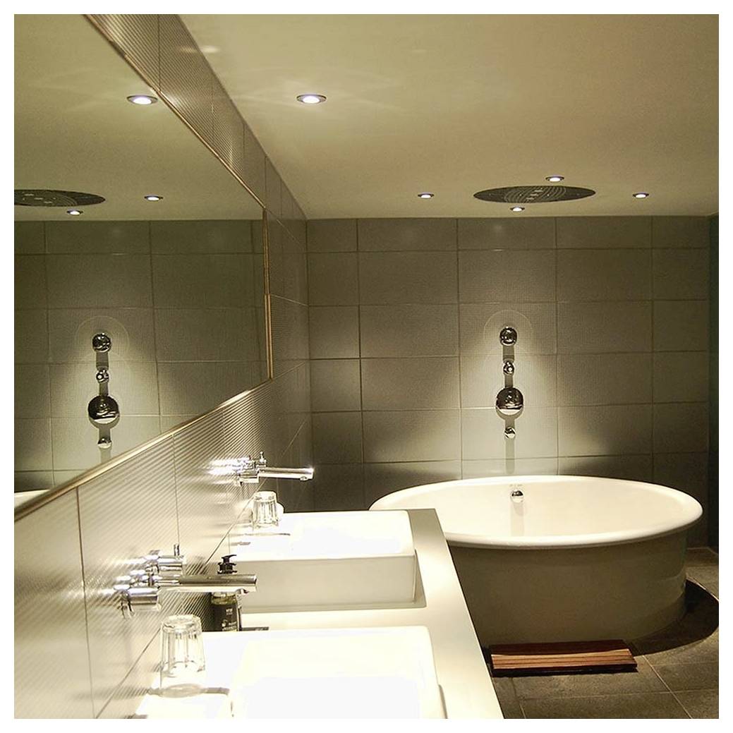 Salle de bains moderne avec une baignoire ronde, double vasques sur un plan de travail, grand miroir, murs carrelés et luminaires au plafond.