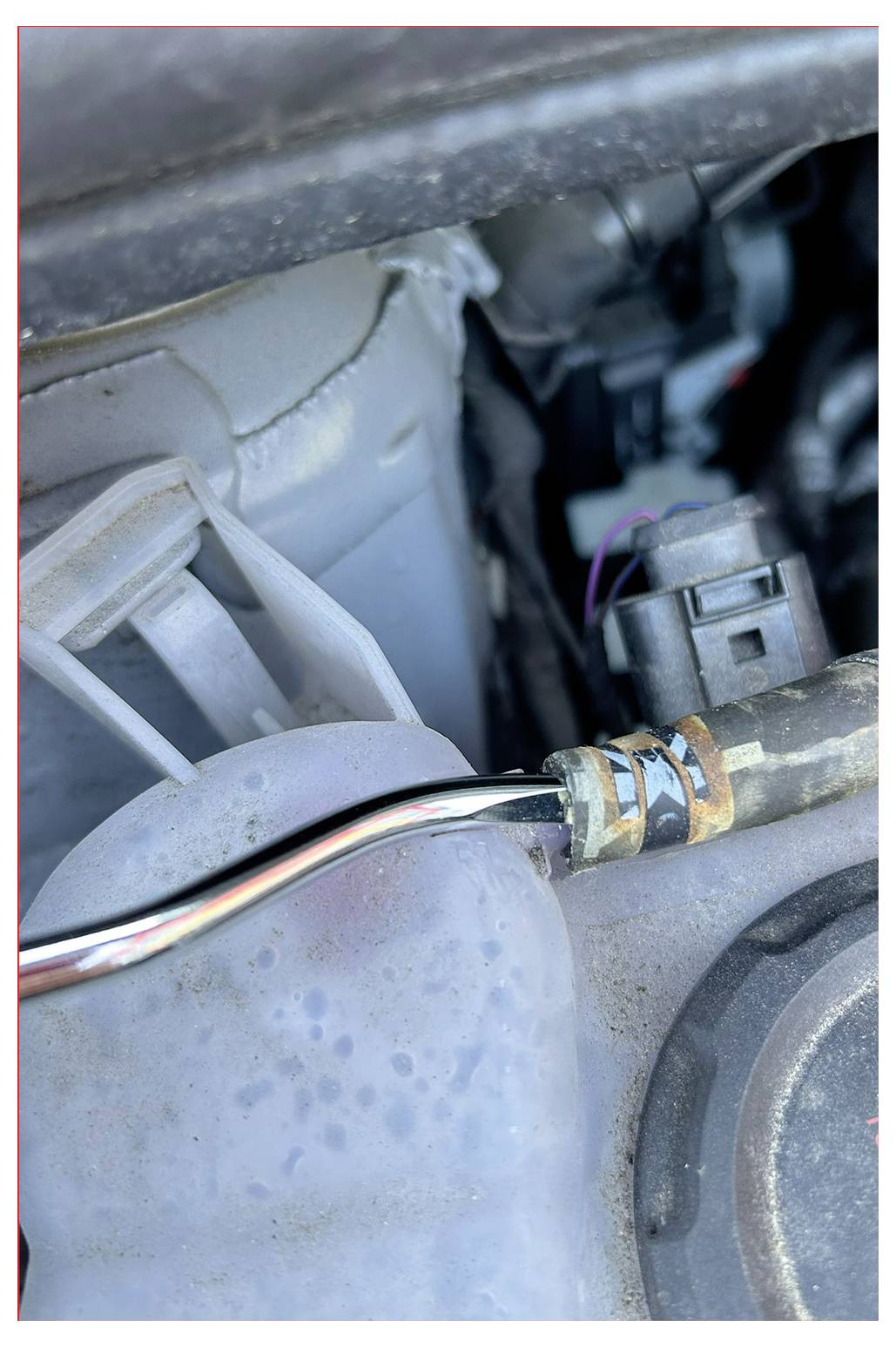 Gros plan d'un composant de moteur automobile avec un connecteur fixé à un cylindre, montrant des pièces en métal et en plastique.