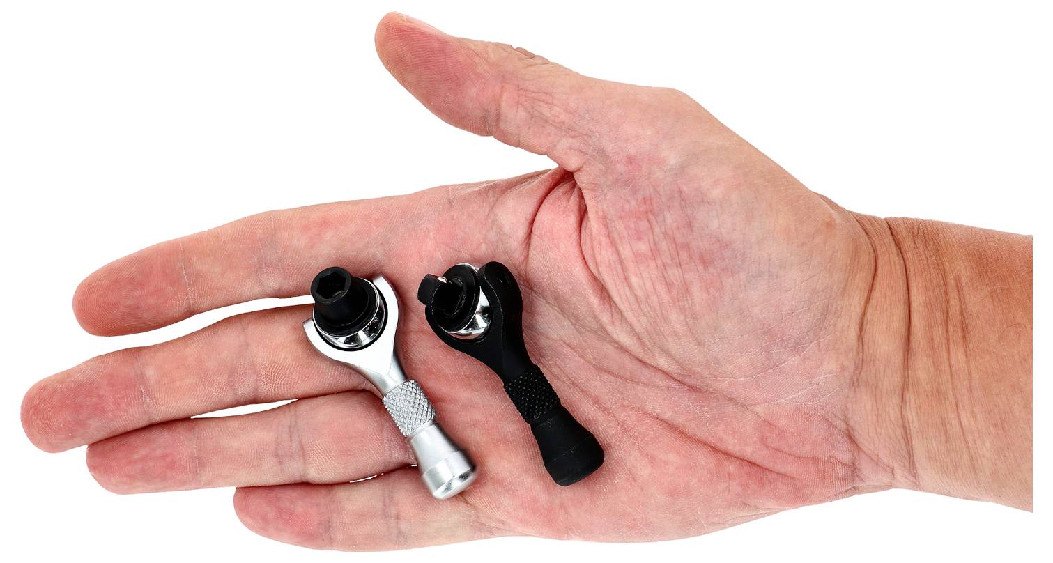 Une main tenant deux petites clés à cliquet, l'une argentée et l'autre noire, mettant en valeur leur taille compacte et leur design de préhension.