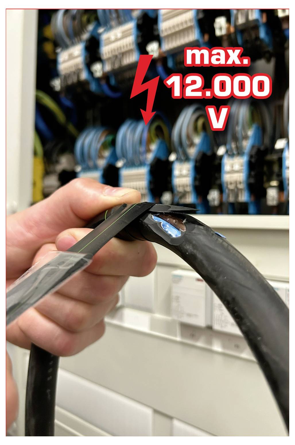 Une personne manipulant un câble noir épais devant un panneau électrique, avec un panneau d'avertissement indiquant « max. 12 000 V ».