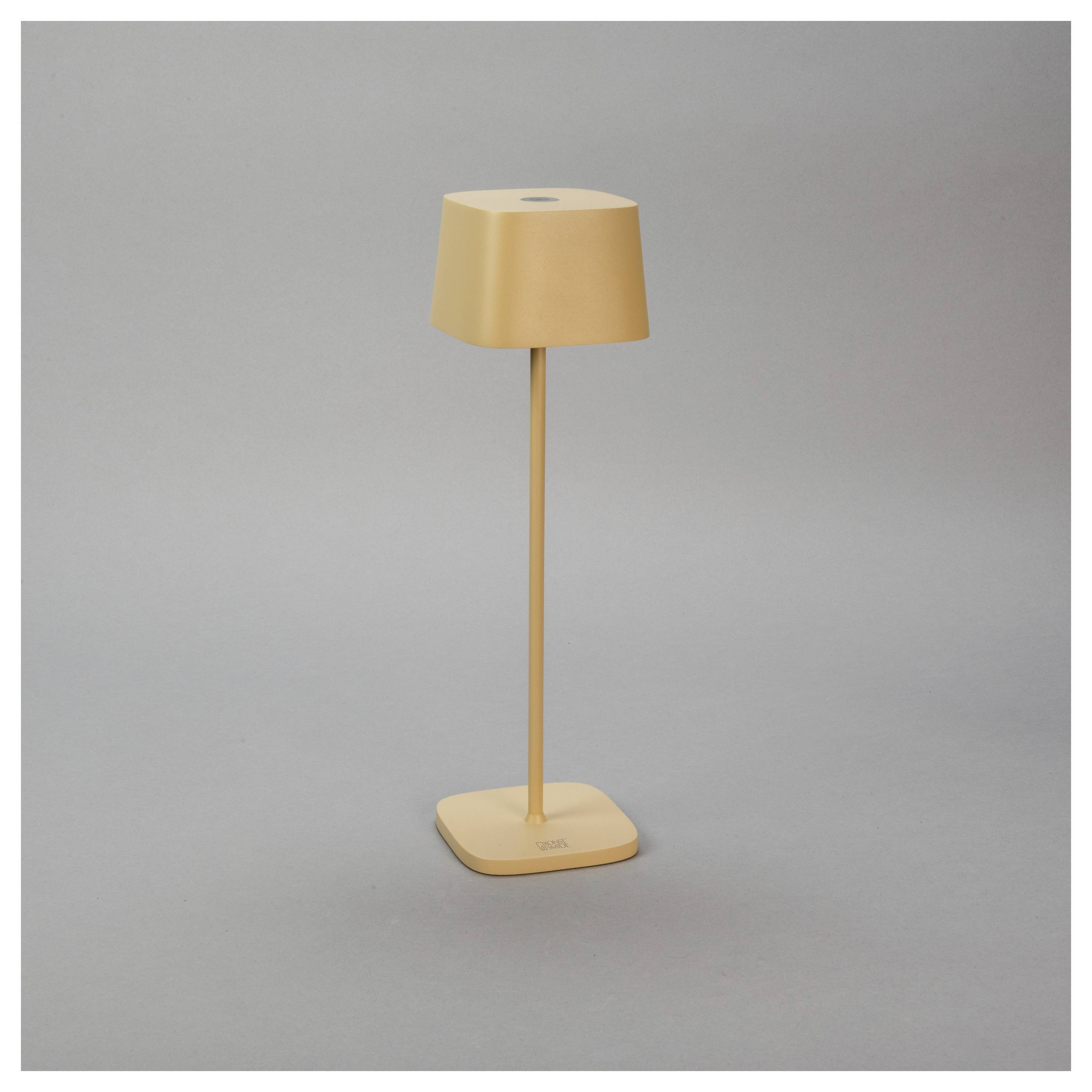 Une lampe de table moderne et sobre en beige, au design minimaliste, posée sur une surface plane devant un fond gris uni.