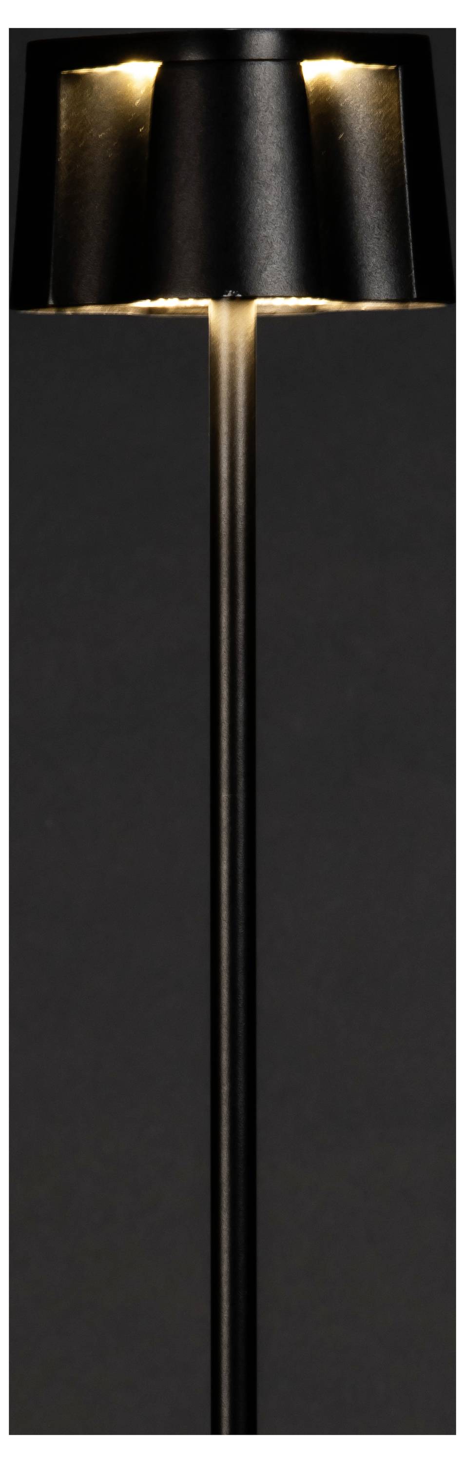 Une lampe sur pied noire et élancée, au design cylindrique épuré, diffuse une lueur chaleureuse depuis son sommet, se détachant sur un fond sombre.