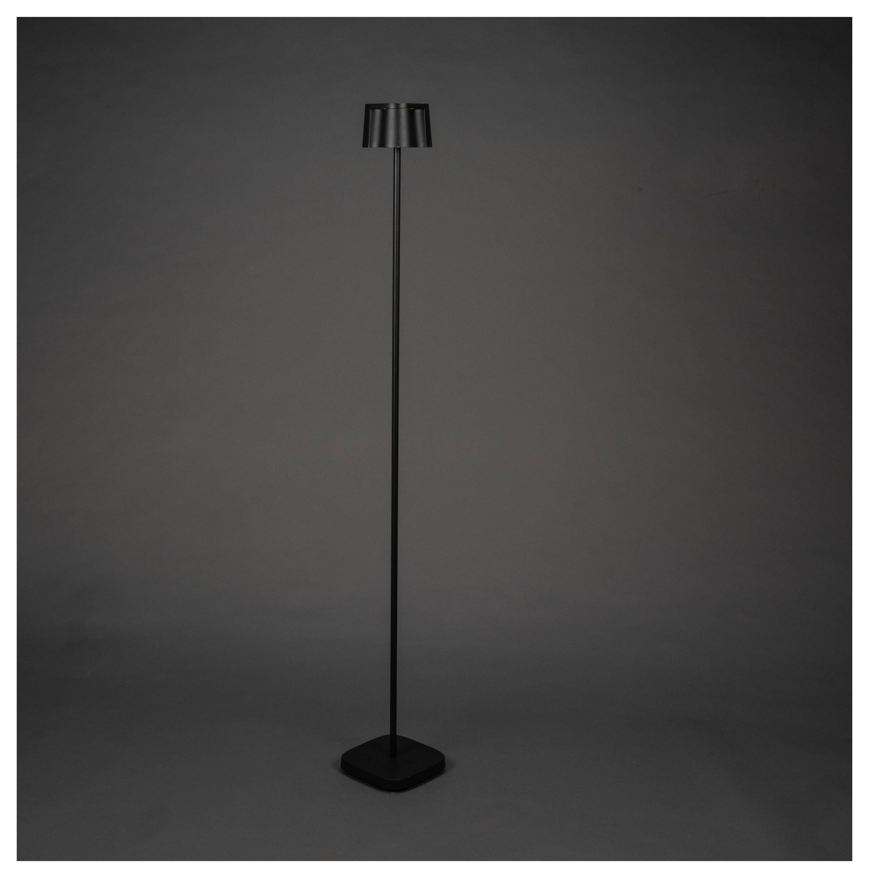Une lampe sur pied moderne et élancée de couleur noire, dotée d'un socle carré et d'un abat-jour cylindrique, se dresse sur un fond sombre.