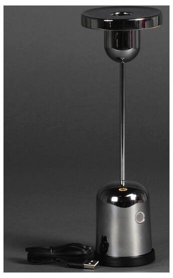 Une lampe de table LED à chargement USB élégante et métallique, dotée d'un bouton tactile, posée à côté de son câble de charge sur un fond sombre.