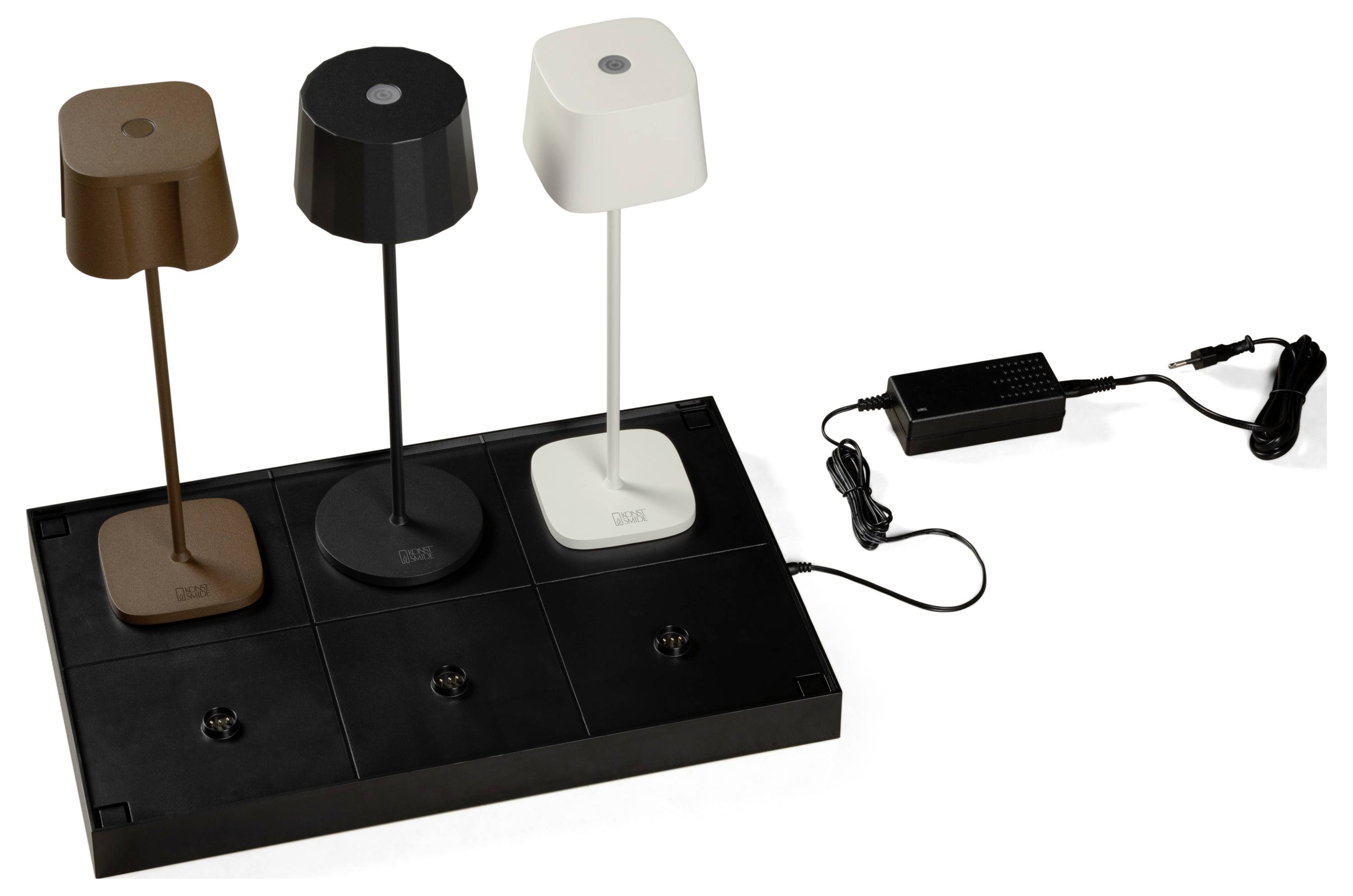 Trois lampes de table de couleurs marron, noir et blanc sont présentées sur un socle noir, connectées à un adaptateur secteur, mettant en valeur leur couleur et leur design.