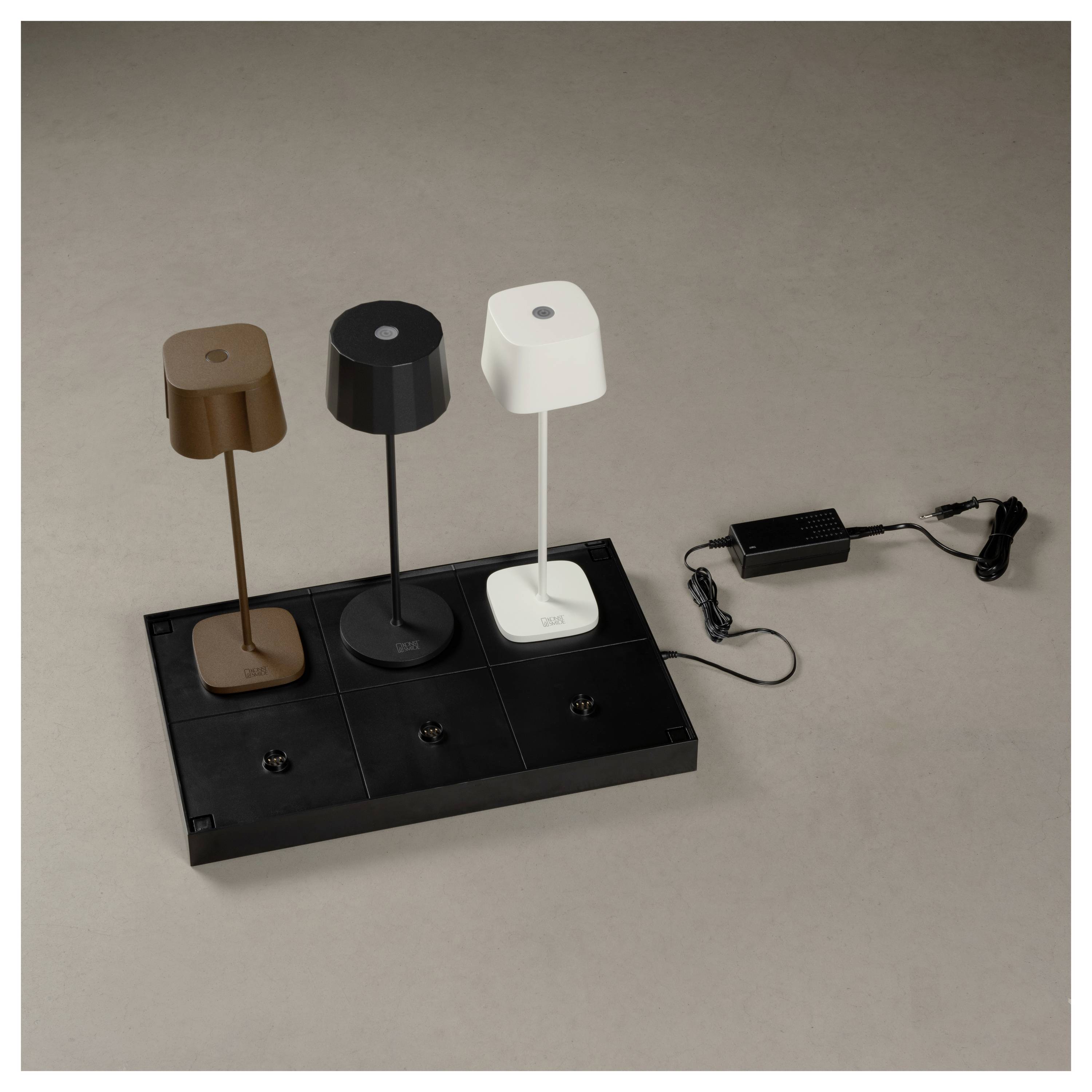 Trois lampes de table modernes en marron, noir et blanc sont placées sur un chargeur sans fil noir, connecté à un adaptateur secteur.