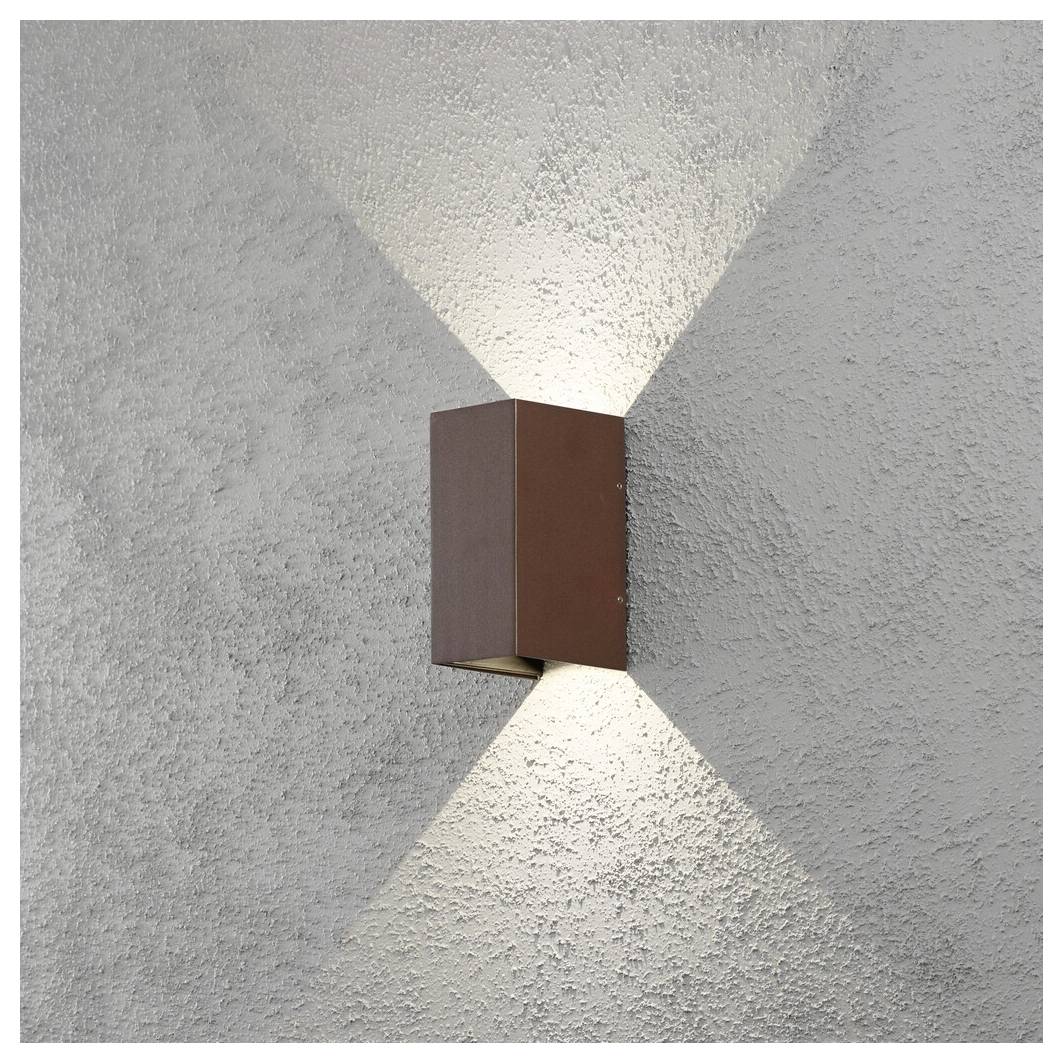 Un luminaire mural projette deux faisceaux de lumière contre un mur gris texturé, l'un vers le haut et l'autre vers le bas, créant un effet décoratif.