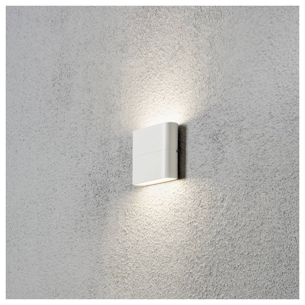 Un luminaire mural moderne de forme carrée émet une lueur douce et diffuse contre un mur gris texturé, créant une esthétique minimaliste.