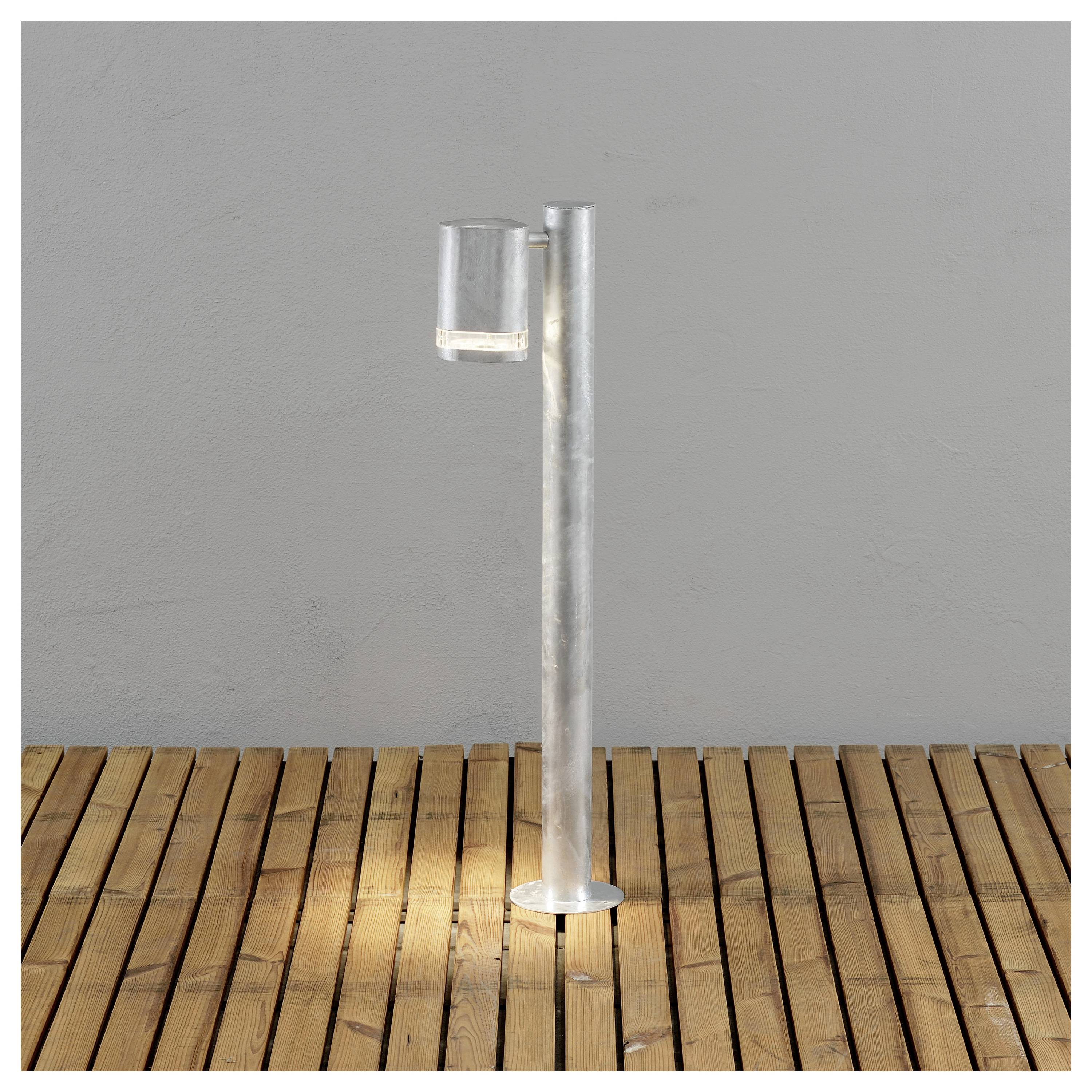 Un verre minimaliste et une tige métallique disposés sur un fond gris et un sol en bois, illustrant des esthétiques industrielles modernes.