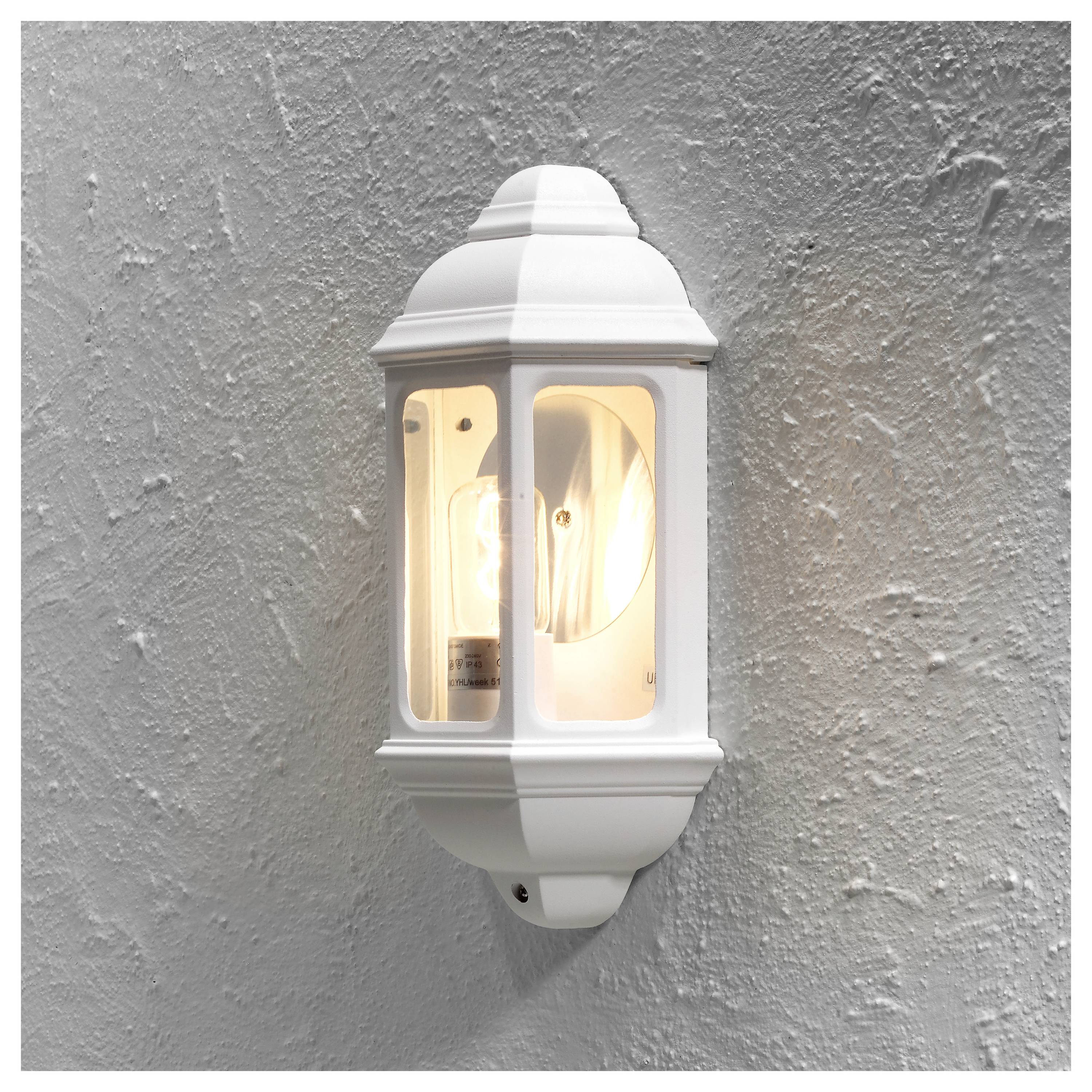 Un luminaire extérieur blanc avec un design simple et classique est fixé sur un mur gris texturé, diffusant une lumière chaleureuse.