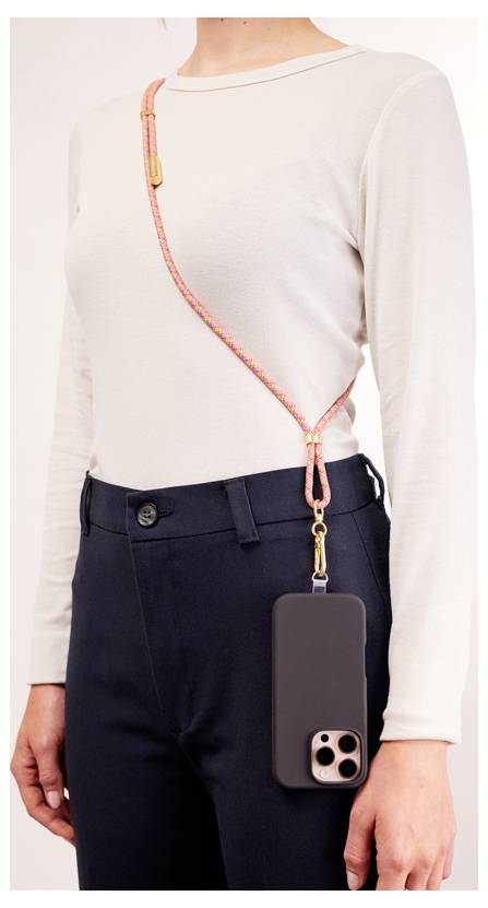 Une personne portant un haut à manches longues léger et un pantalon foncé utilise une bandoulière de téléphone colorée attachée à une coque de smartphone.