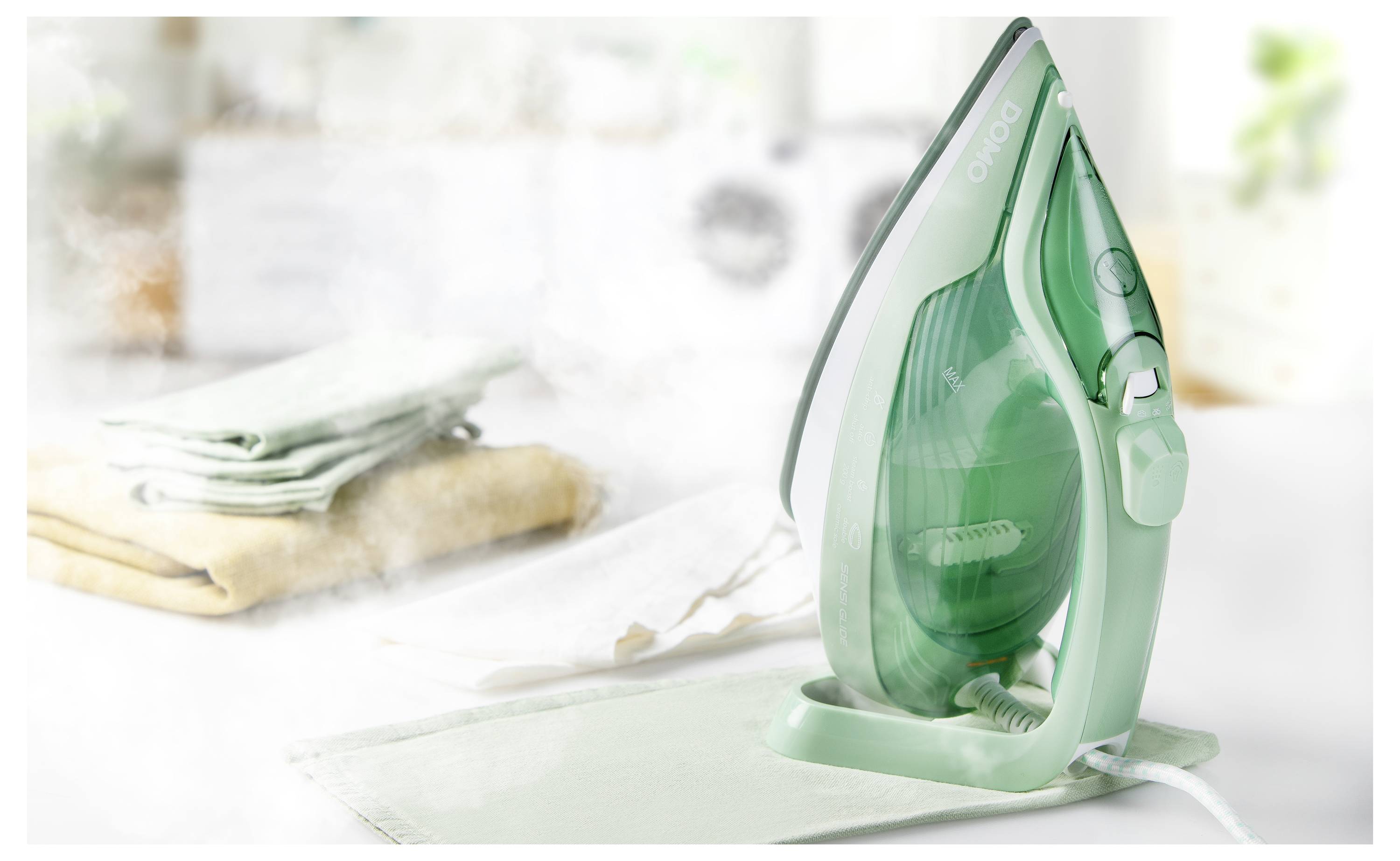 Un fer à repasser libérant de la vapeur est posé sur une planche à repasser, avec une pile de vêtements pliés en arrière-plan, suggérant le repassage de vêtements.