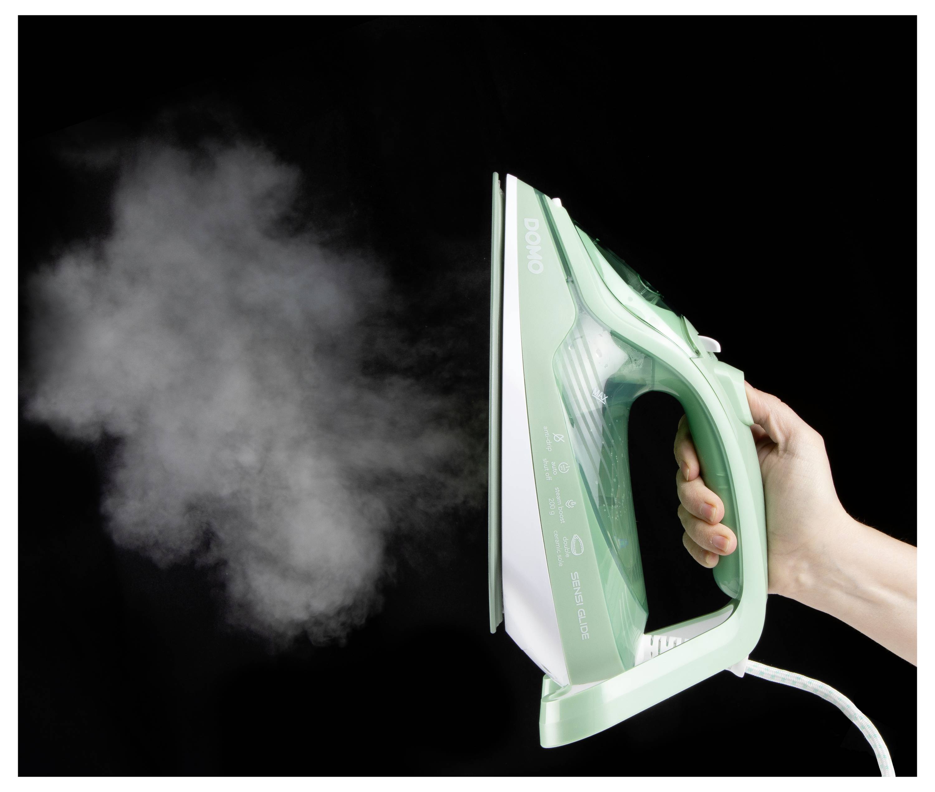 Une main tient un fer à repasser vert fumant contre un fond noir, démontrant la fonction vapeur et le design ergonomique.
