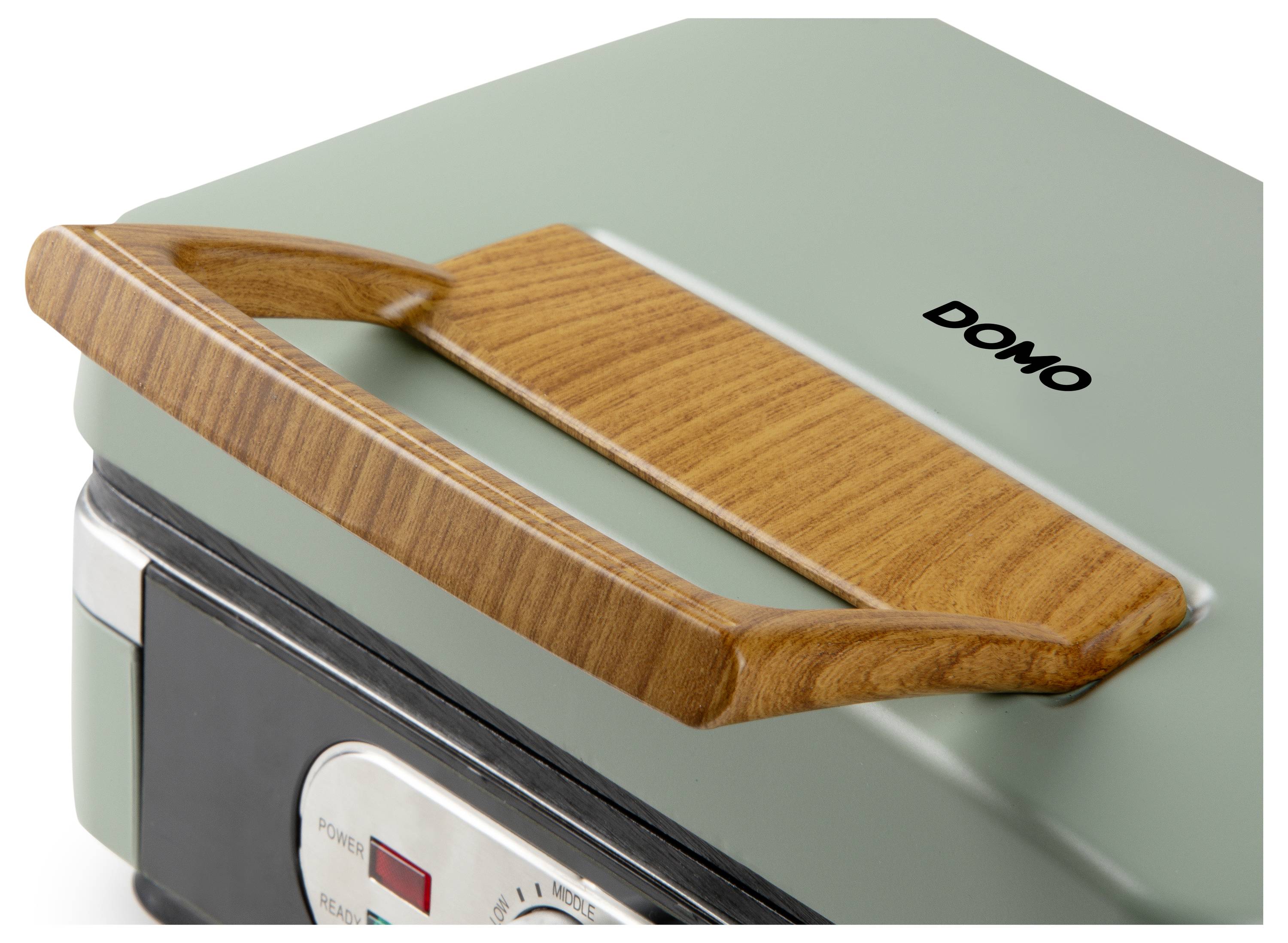 Un gros plan d'un appareil de cuisson vert avec une poignée en bois et un panneau de commande argenté. Le nom de la marque 'DOMO' est visible en haut.