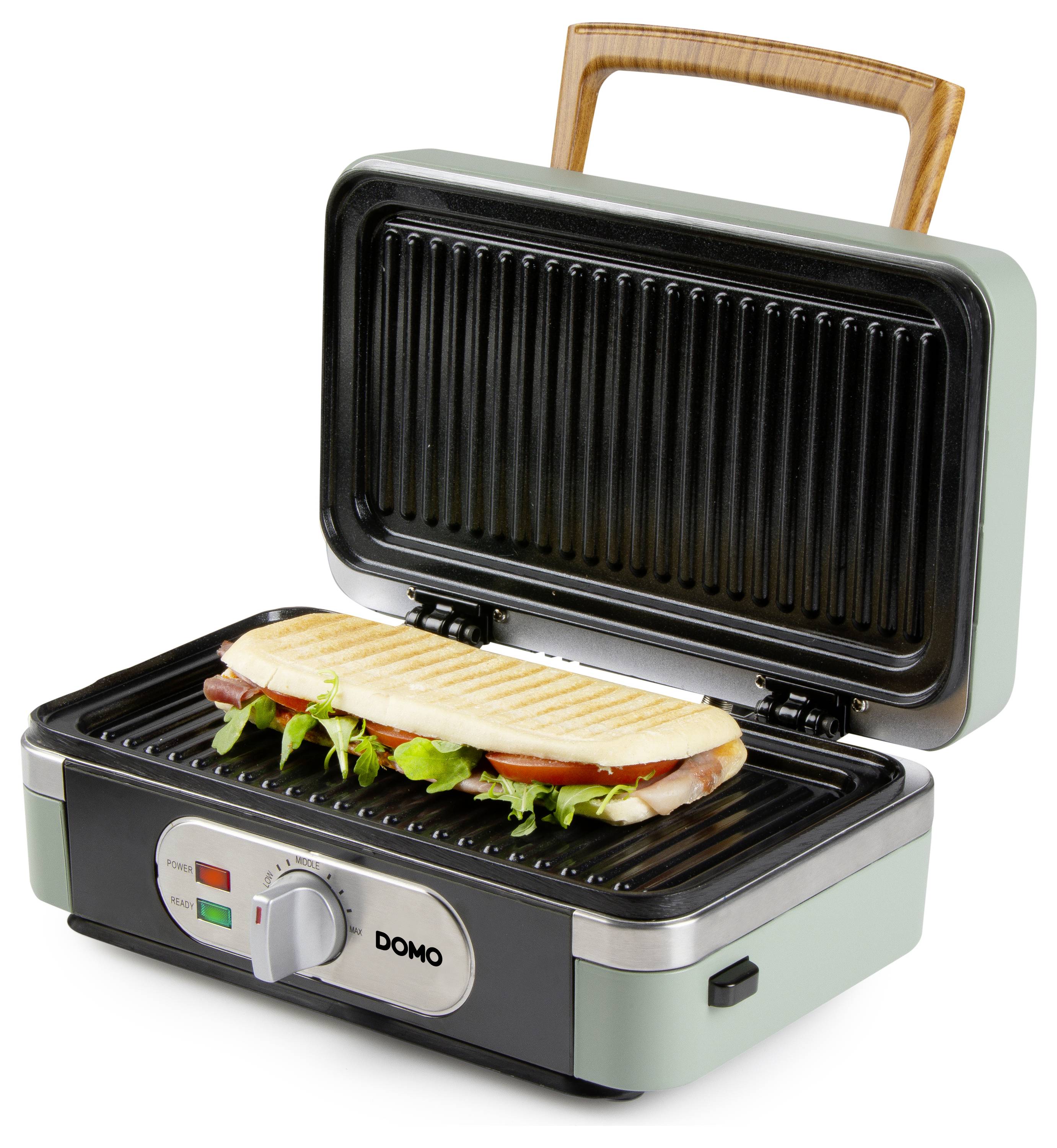 Une presse à panini avec un couvercle à moitié ouvert, faisant griller un sandwich garni de verdure et de charcuterie. Le panneau de commande affiche un indicateur de chauffage.
