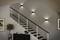 Un escalier moderne aux marches noires et blanches, éclairé par des luminaires muraux. Un petit placard et une plante sont situés à la base.