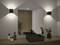 Un meuble-lavabo de salle de bain moderne présente un lavabo carré noir, un robinet et de petites plantes sur un comptoir en bois, sous des appliques murales rectangulaires.