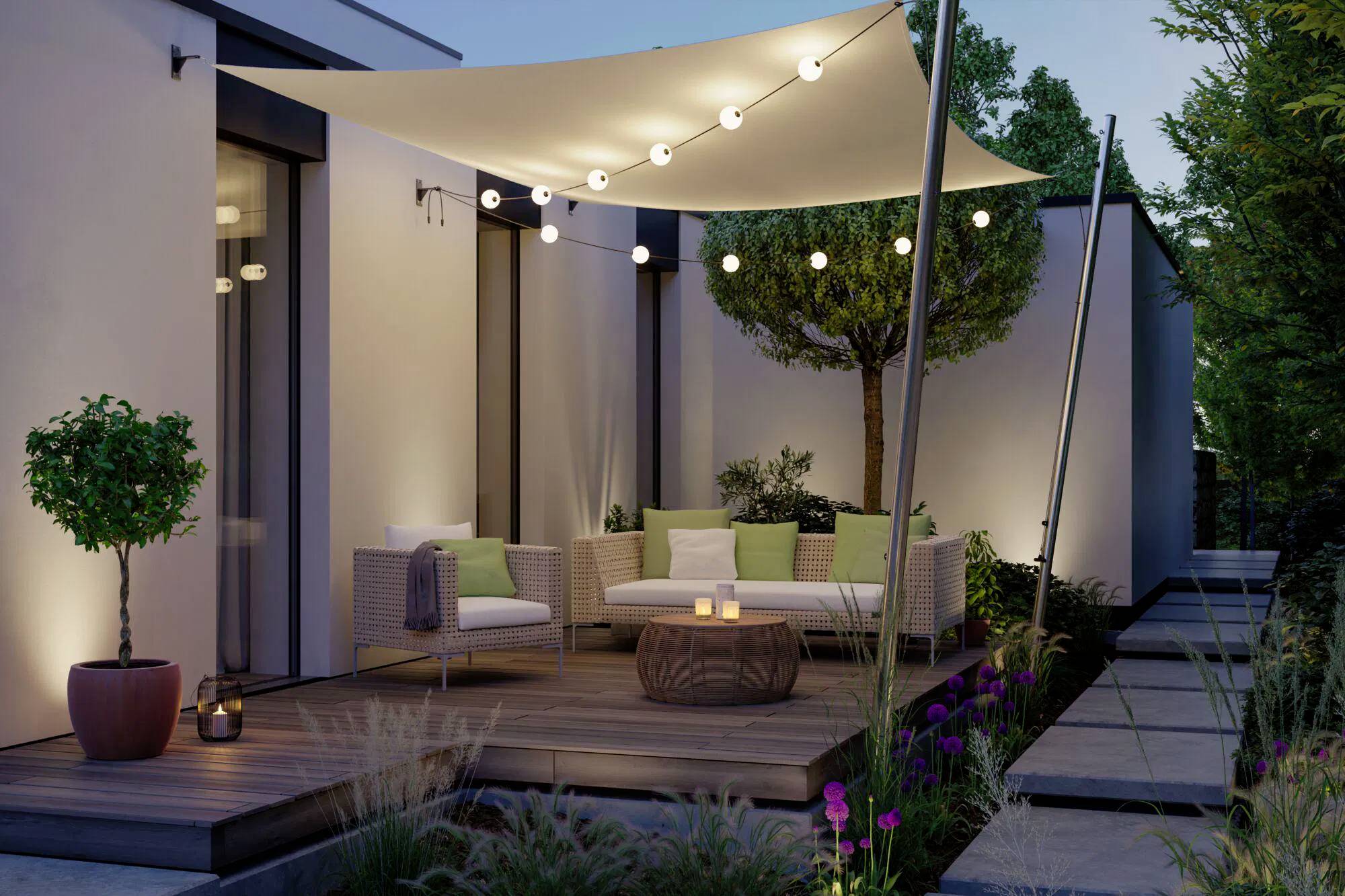 Terrasse extérieure moderne avec un auvent, des guirlandes lumineuses et un espace de séjour entouré de plantes, créant une ambiance chaleureuse en soirée.