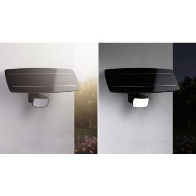 Un luminaire de sécurité équipé d'un panneau solaire fixé à un mur, présenté de jour et illuminé la nuit, avec un décor de jardin en arrière-plan.