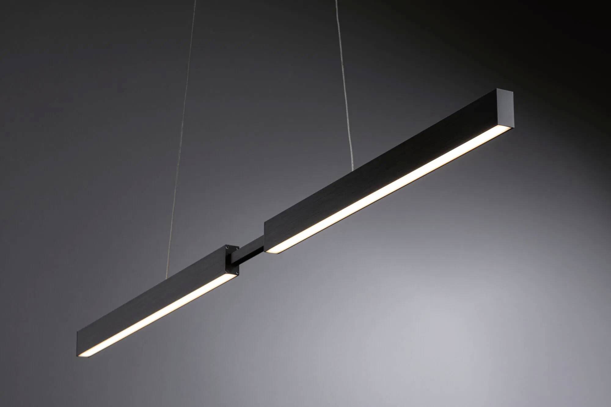 Un luminaire suspendu linéaire élégant et moderne, avec une finition noire, suspendu par des fils fins, diffusant une lueur douce et uniforme dans une pièce sombre.