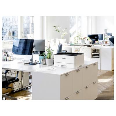 Un espace de bureau ouvert et moderne avec des bureaux, des ordinateurs et une imprimante Canon posée sur un meuble. De grandes fenêtres offrent une lumière naturelle et une vue sur la ville.